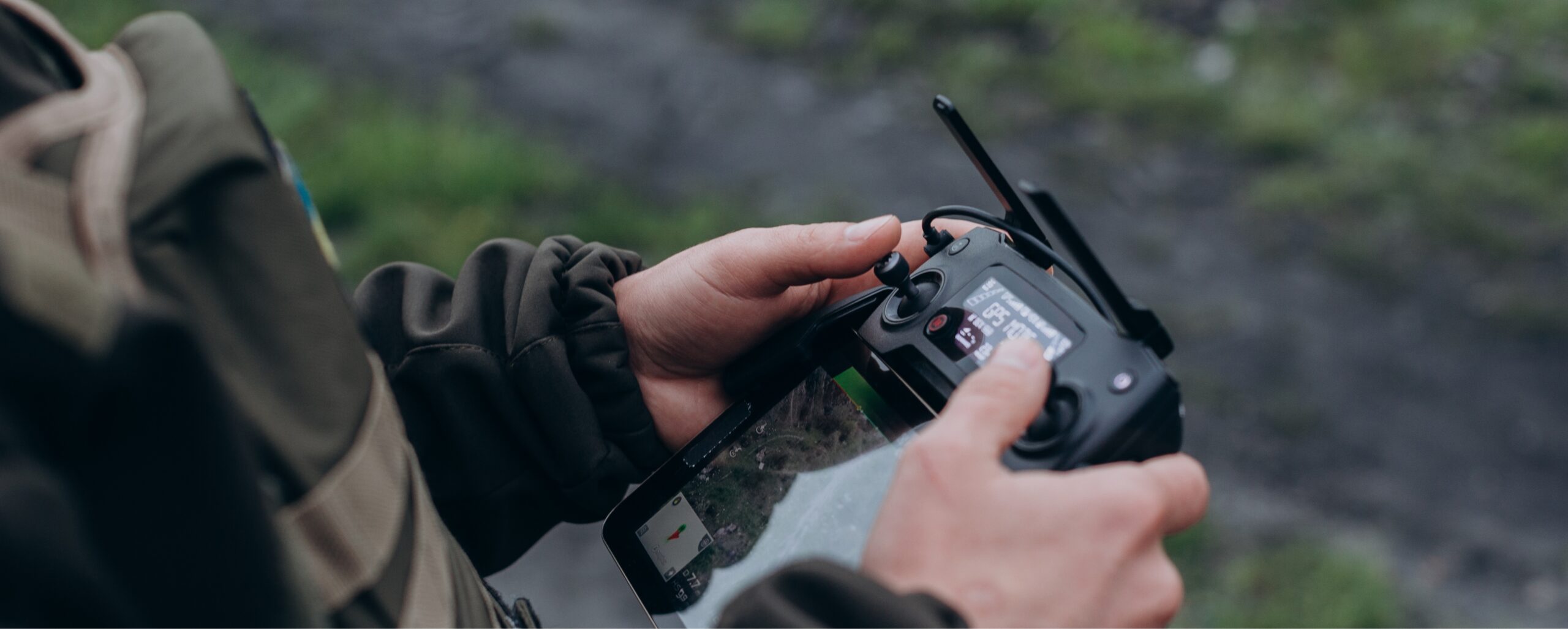 Person holding and operating a DJI remote controller outdoors, focusing on controlling a military drone
