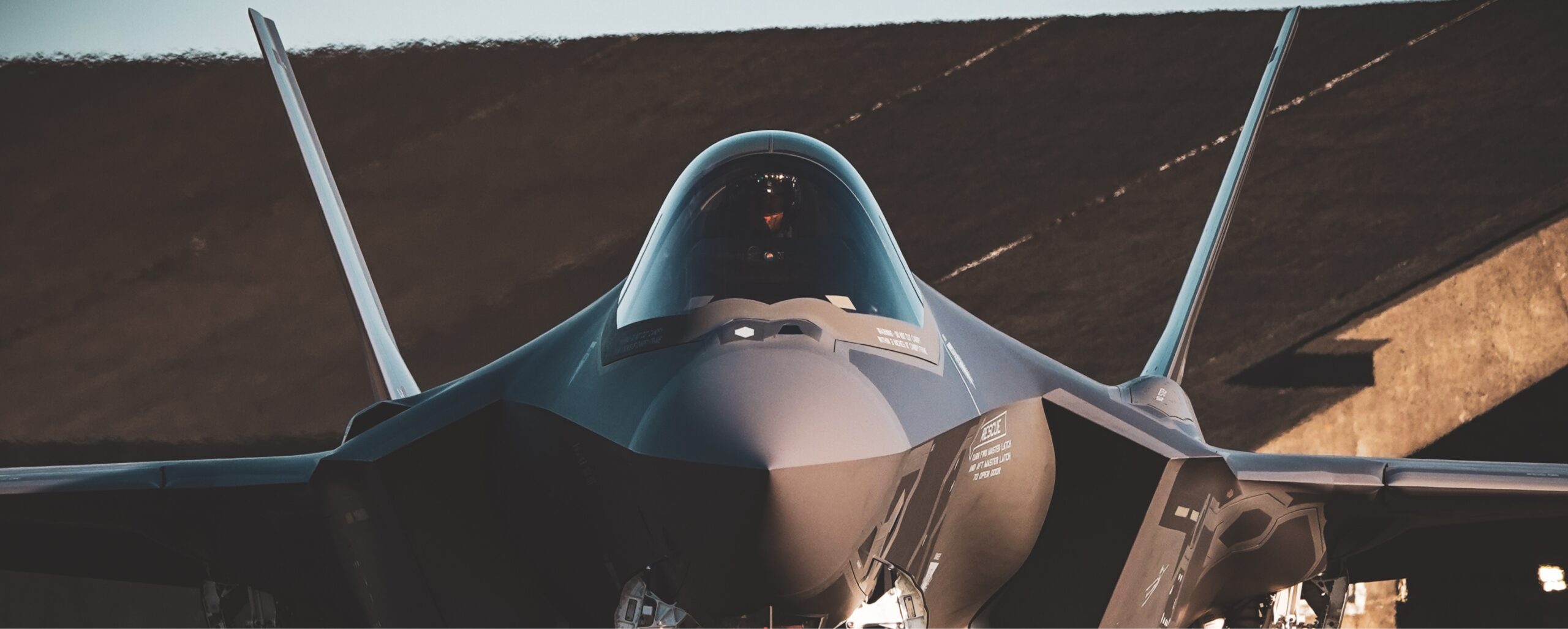Front view of a military stealth fighter jet parked with its cockpit canopy closed and twin vertical stabilizers visible.