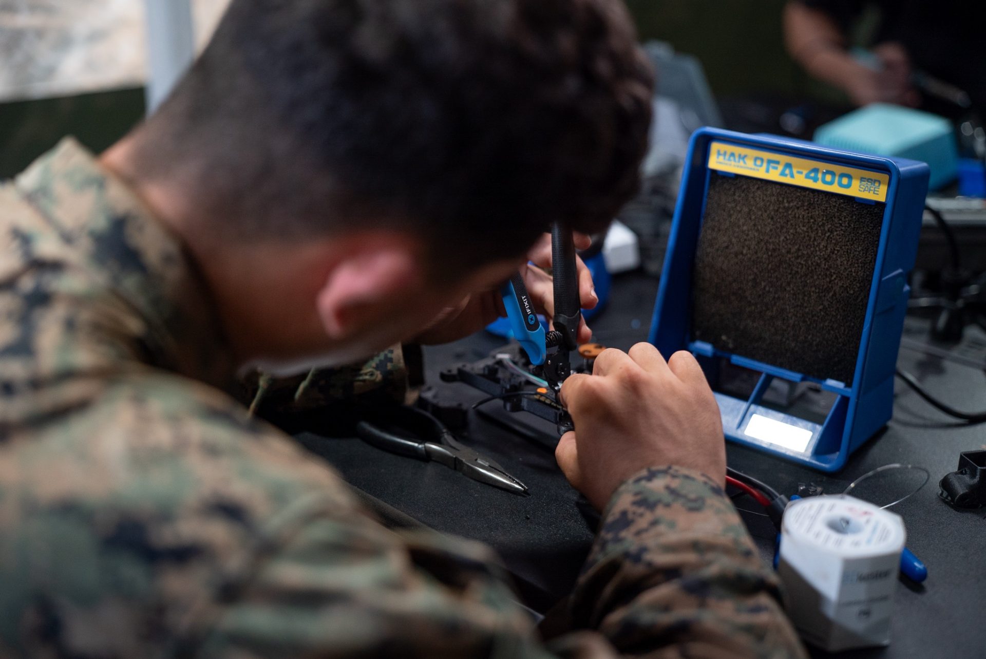 Uniformed operator soldering small drone electronics at a hands-on FPV build course workbench